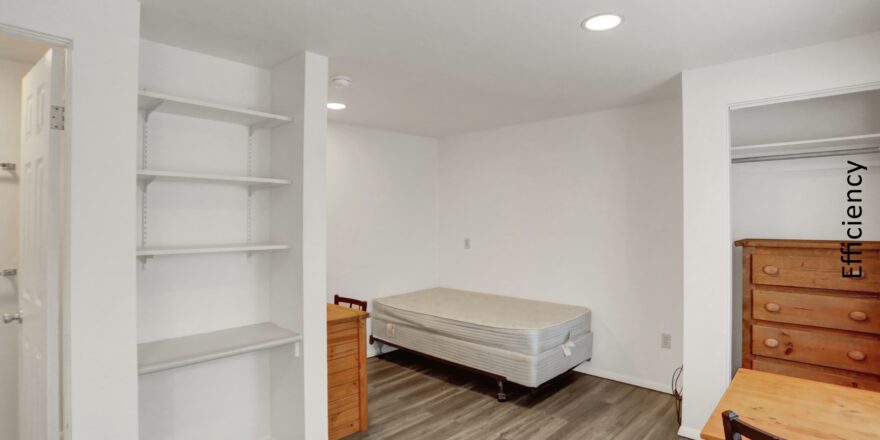 an empty room with a bed, desk and shelves