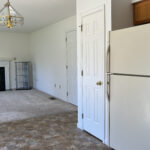 view of kitchen cabinets, refrigerator, pantry door, and living room carpet and decorative fireplace, with a golden chandelier light fixture on ceiling