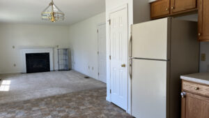 view of kitchen cabinets, refrigerator, pantry door, and living room carpet and decorative fireplace, with a golden chandelier light fixture on ceiling