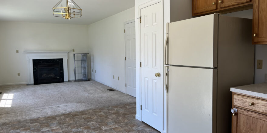 view of kitchen cabinets, refrigerator, pantry door, and living room carpet and decorative fireplace, with a golden chandelier light fixture on ceiling