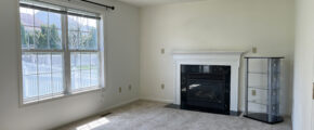 an empty living room with a fireplace and large windows