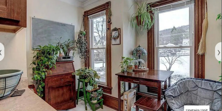 upstairs unit dining area next to kitchen with two windows, white walls, and hard flooring