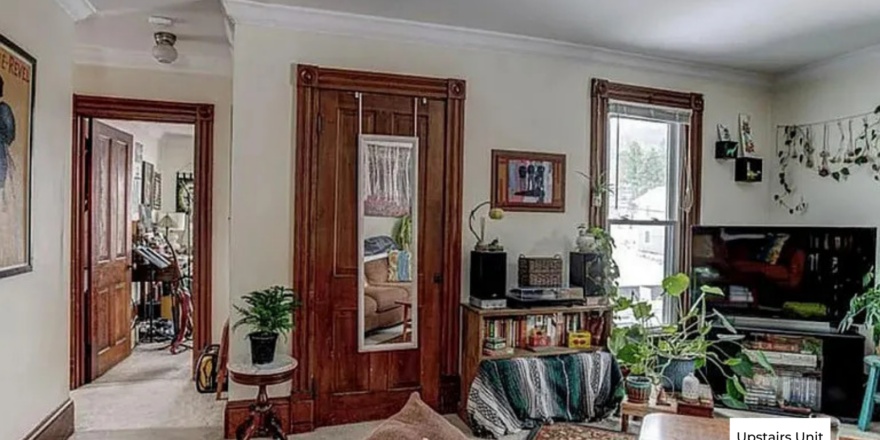 upstairs unit living room with white walls, a window in the corner, and light carpeting