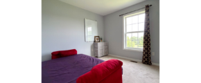 a carpeted bedroom with a futon, dresser and window