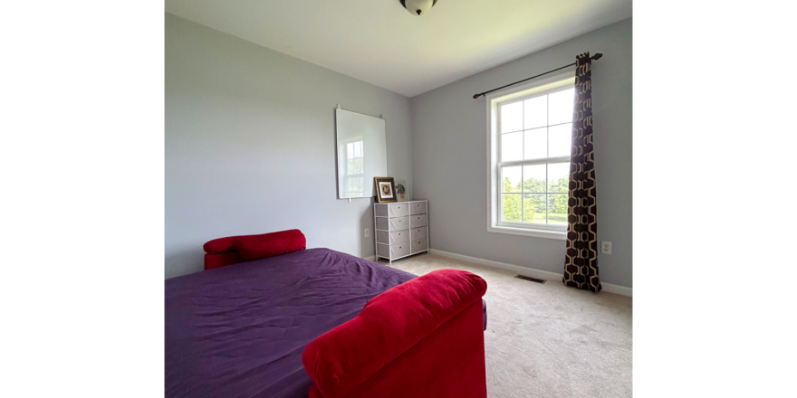 a carpeted bedroom with a futon, dresser and window