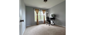 a carpeted bedroom with a large window, desk and chair in it