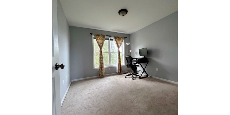 a carpeted bedroom with a large window, desk and chair in it