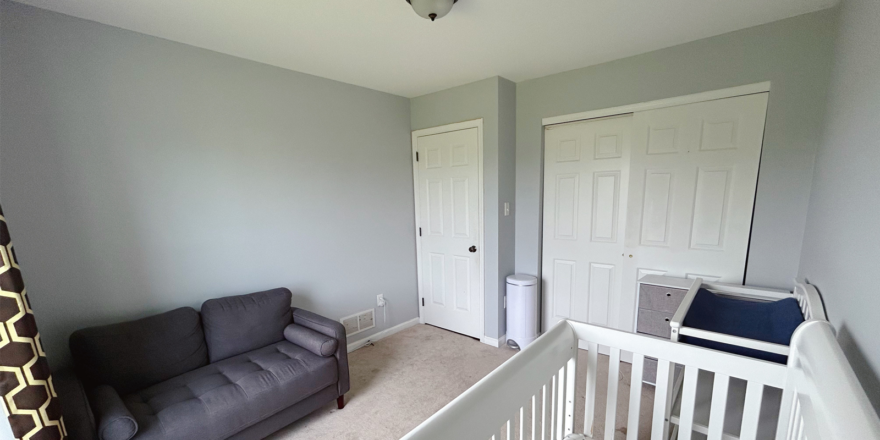 a carpeted bedroom with a couch, crib, and a closet