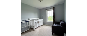 a carpeted bedroom with a crib, chair, and window