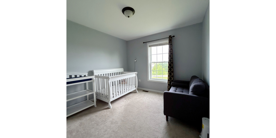 a carpeted bedroom with a crib, chair, and window