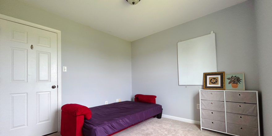 a carpeted bedroom with a futon bed, dresser and mirror