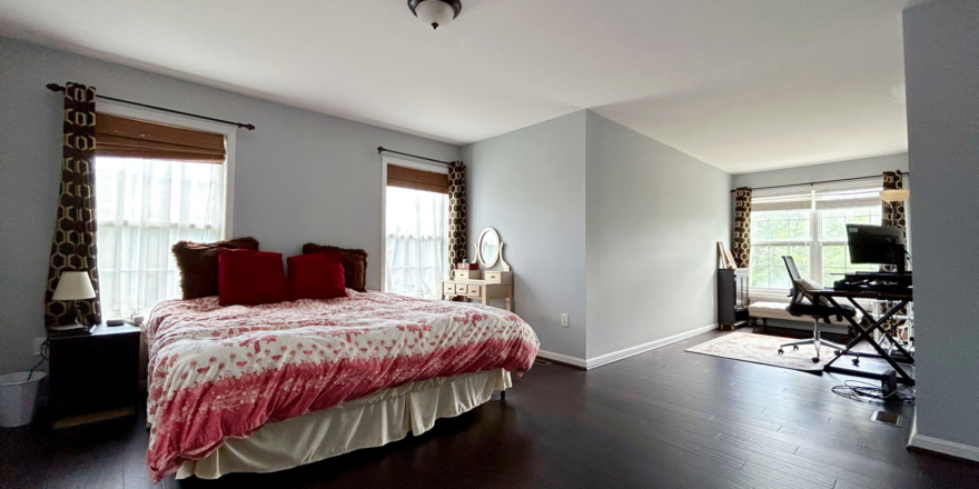 a bedroom with a bed, desk and two windows