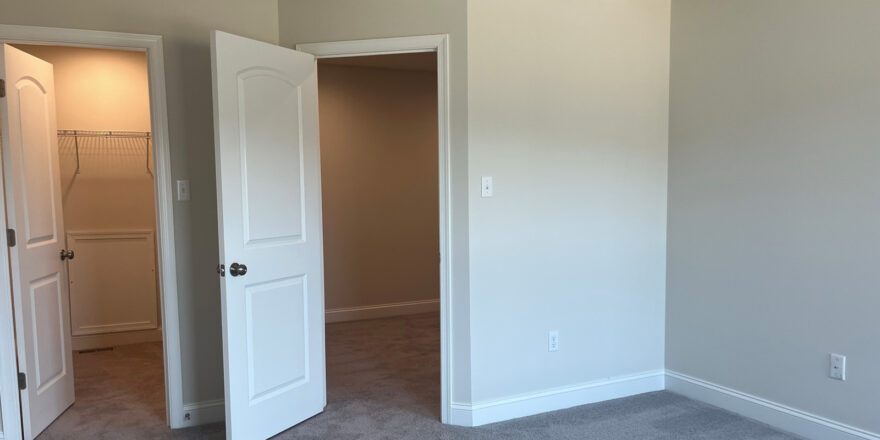 an empty room with two white doors open, one of which is a walk in closet