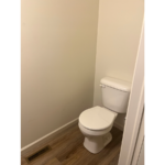 a white toilet sitting in a bathroom next to a wooden floor