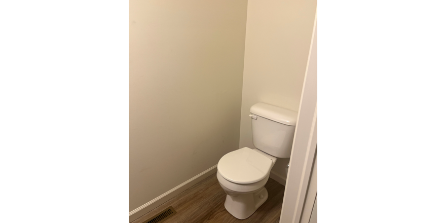 a white toilet sitting in a bathroom next to a wooden floor