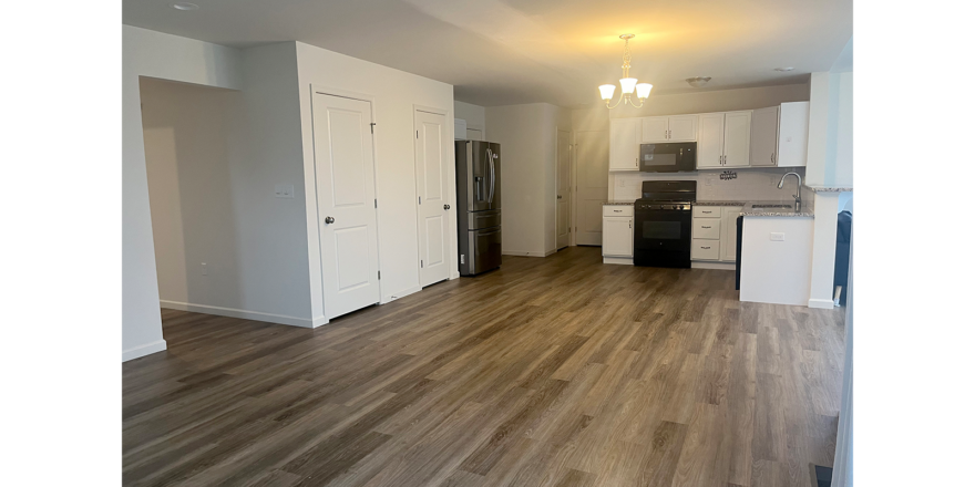 an empty kitchen with white cabinets and wood floors