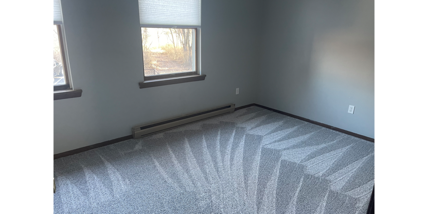 an empty bedroom with a carpeted floor and two windows