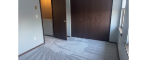 a carpeted empty bedroom with one closet closed behind two bi-fold doors