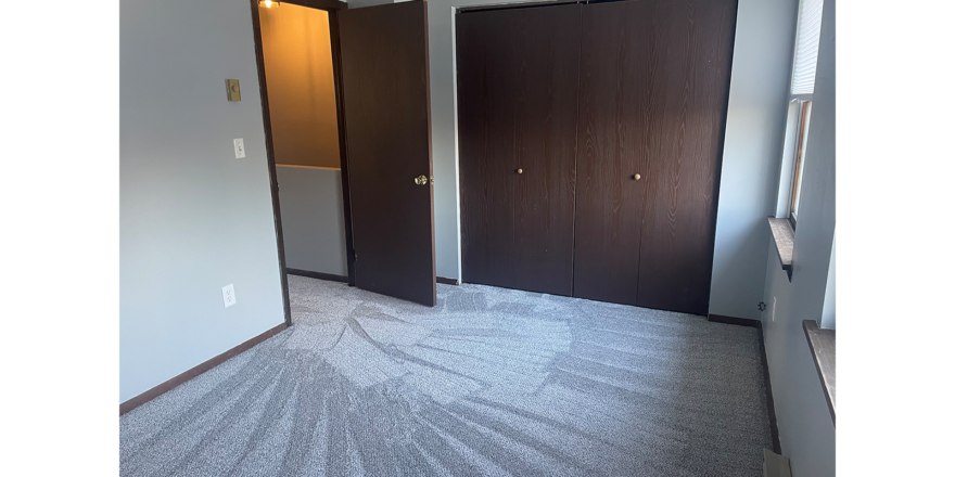 a carpeted empty bedroom with one closet closed behind two bi-fold doors