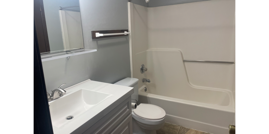 a bathroom with a white toilet sitting between a white bath tub and white sink with vanity
