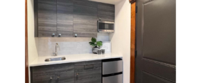 a small kitchenette with stainless steel mini fridge and gray wood cabinets