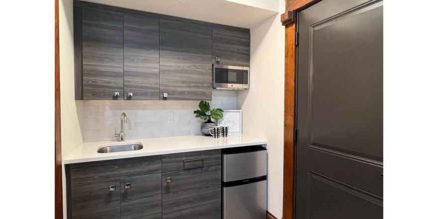 a small kitchenette with stainless steel mini fridge and gray wood cabinets