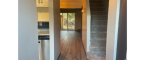 an empty hallway with hardwood floors leading to a kitchen and living room