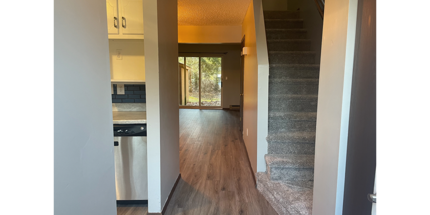 an empty hallway with hardwood floors leading to a kitchen and living room