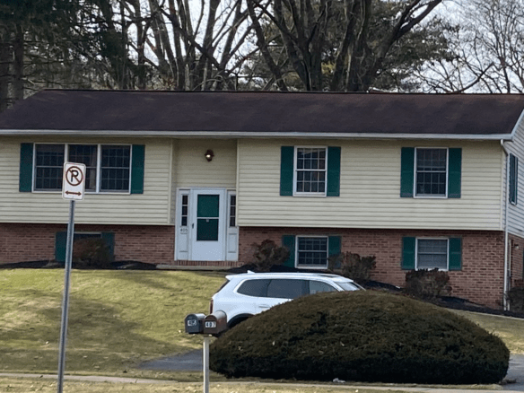 Exterior of house with a shingled roof, white door, emerald green shutters,Light tan siding on the top half and brick on the bottom half