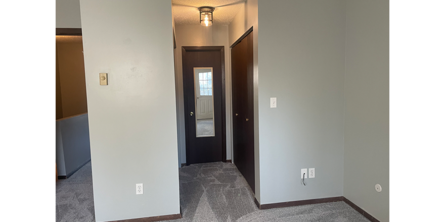 an empty room with two bi-fold closet doors, a door to the bathroom, and a carpeted floor