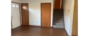 an empty living room with wood floors and white walls and stairs leading to bedrooms