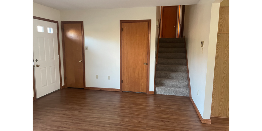 an empty living room with wood floors and white walls and stairs leading to bedrooms