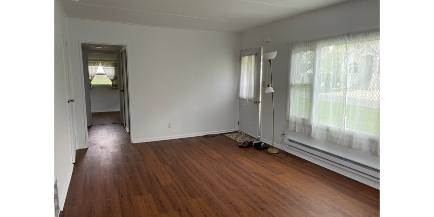 an empty room with white walls, brown LVP floors, a large window, and entry doorway