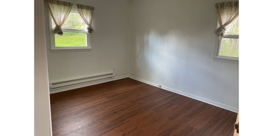 empty room with white walls, LVP brown wood floors, and two windows