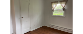 an empty room with a white door, window, white walls. and brown LVP flooring