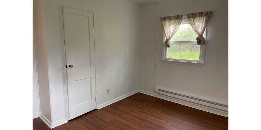 an empty room with a white door, window, white walls. and brown LVP flooring