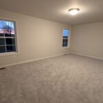 an empty room with carpet and two windows