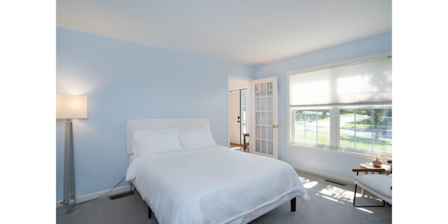 a bedroom with a white bed and two windows