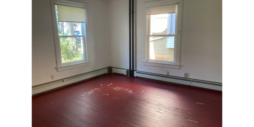 an empty room with two windows and a hard wood floor