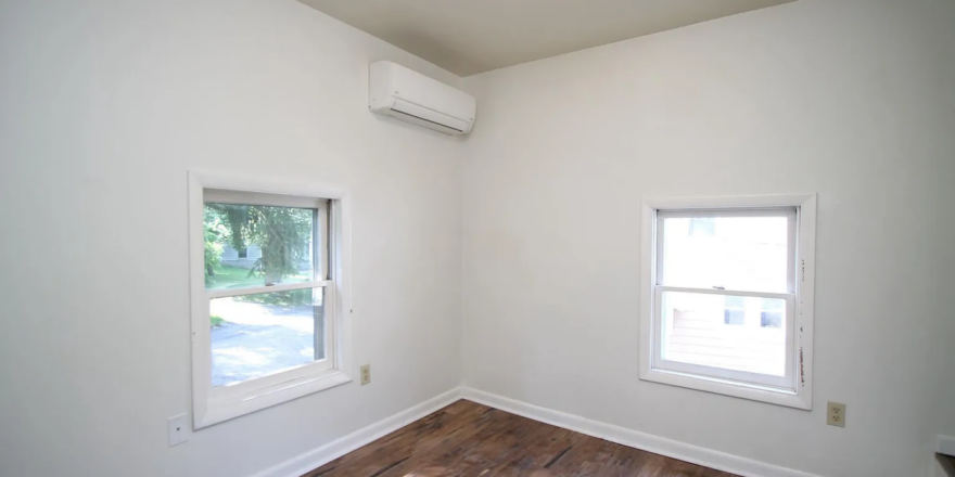 an empty room with two windows and a hard wood floor