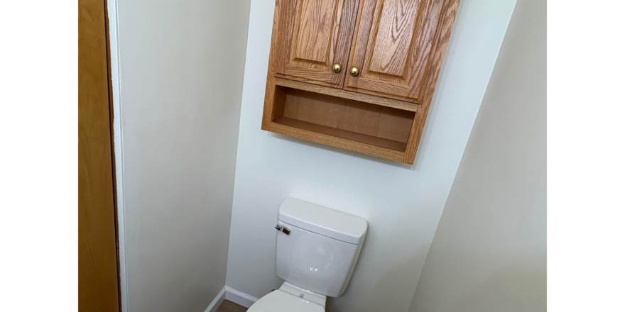 a bathroom with a toilet and wooden cabinet above it