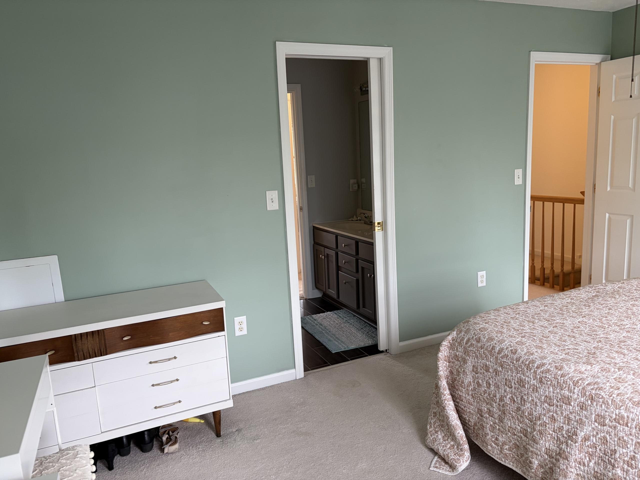 Bedroom with white dresser, bed, and open door to bathroom