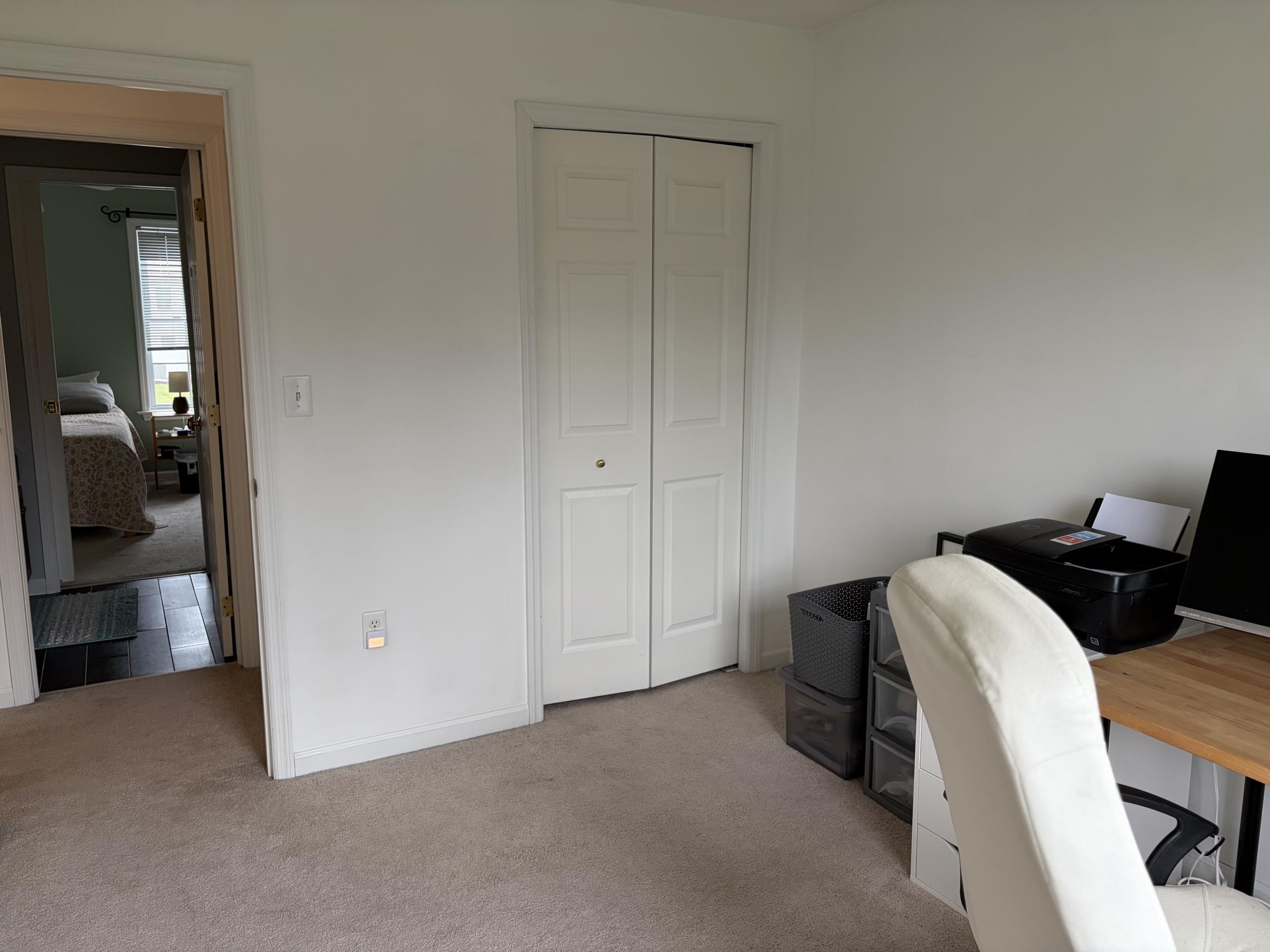 Empty room with white walls, carpet, and a desk with a printer