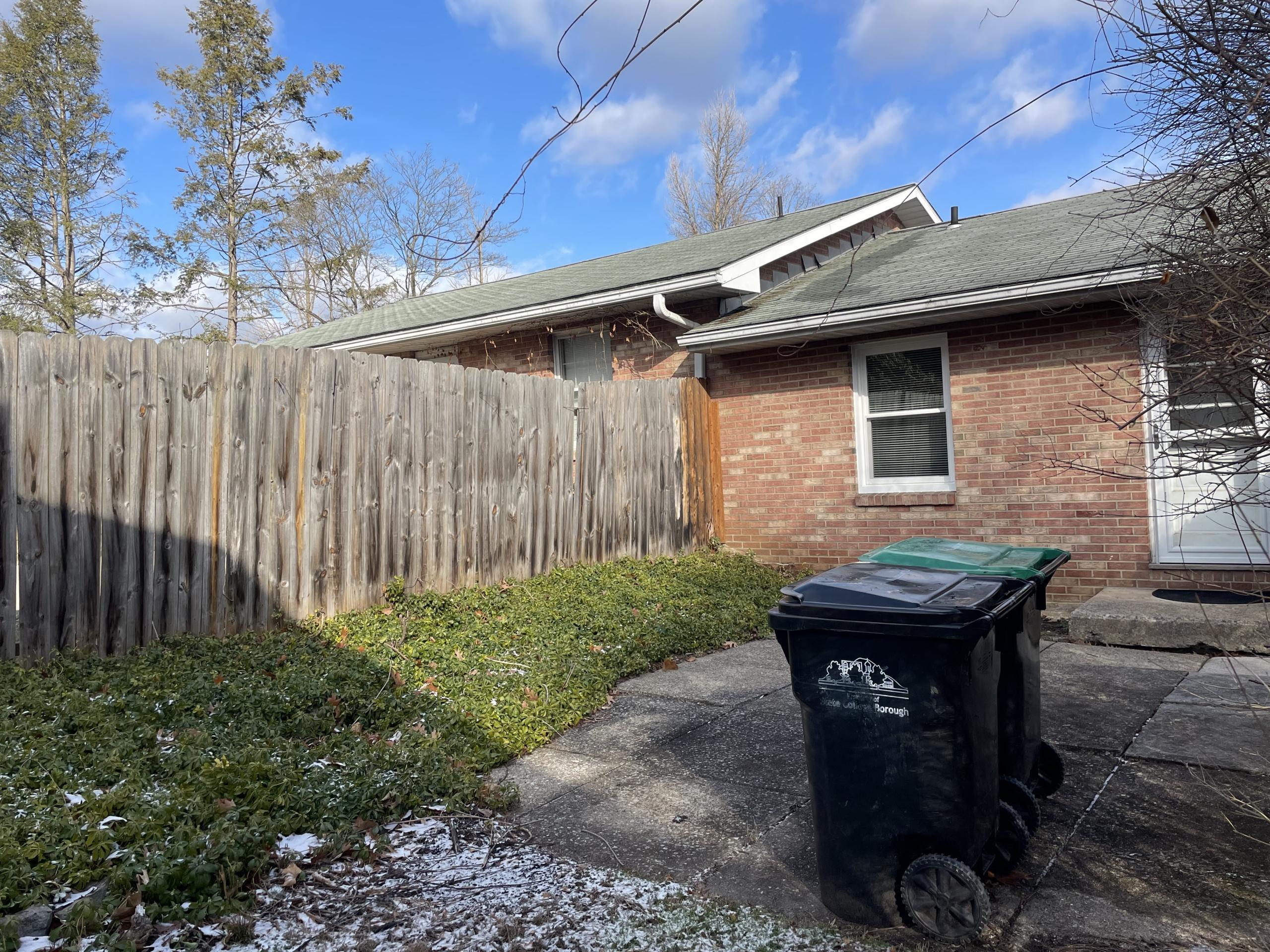 Brick house with trash bins and wooden fence