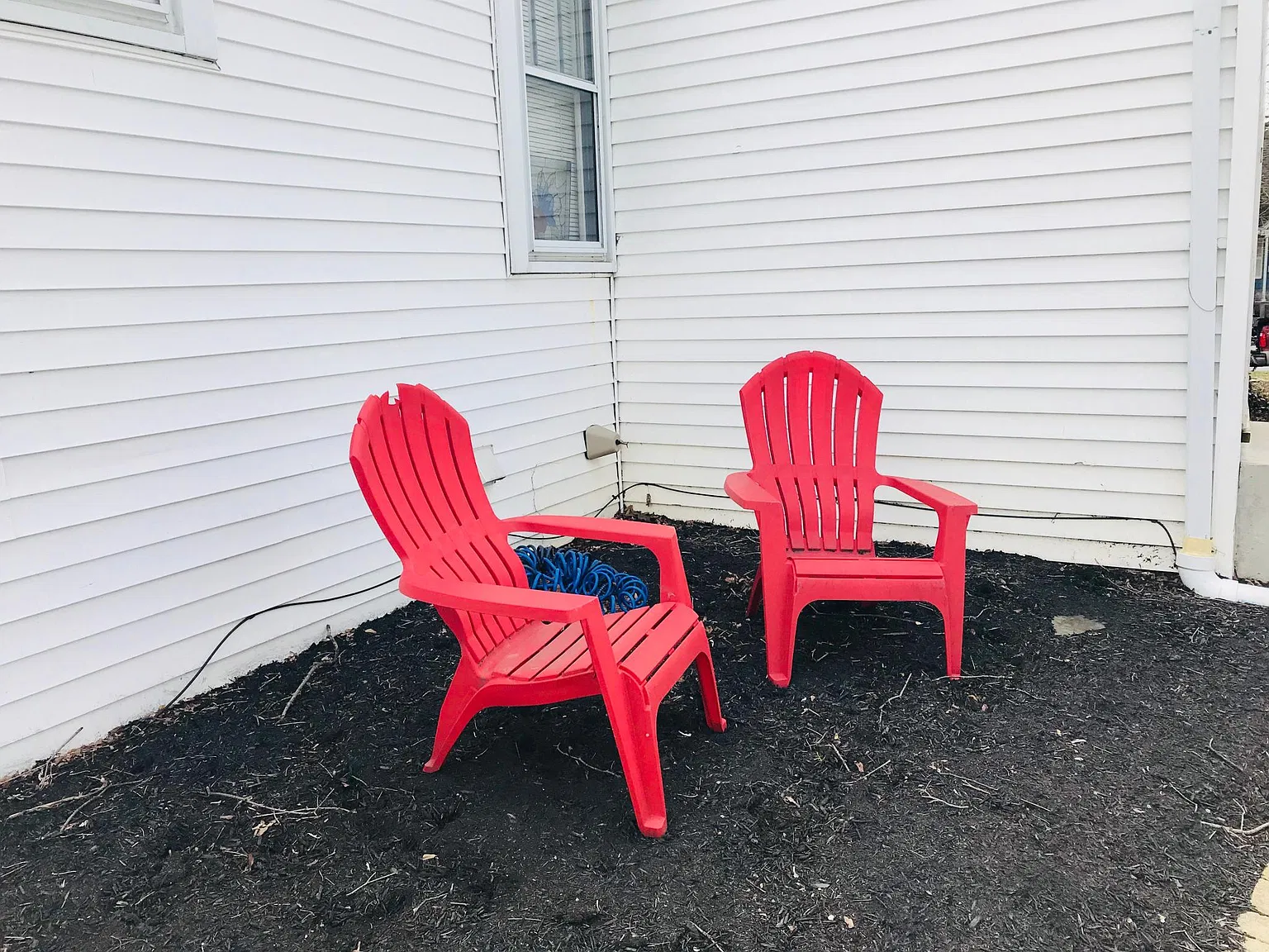 Two red Adirondack chairs on dark mulch